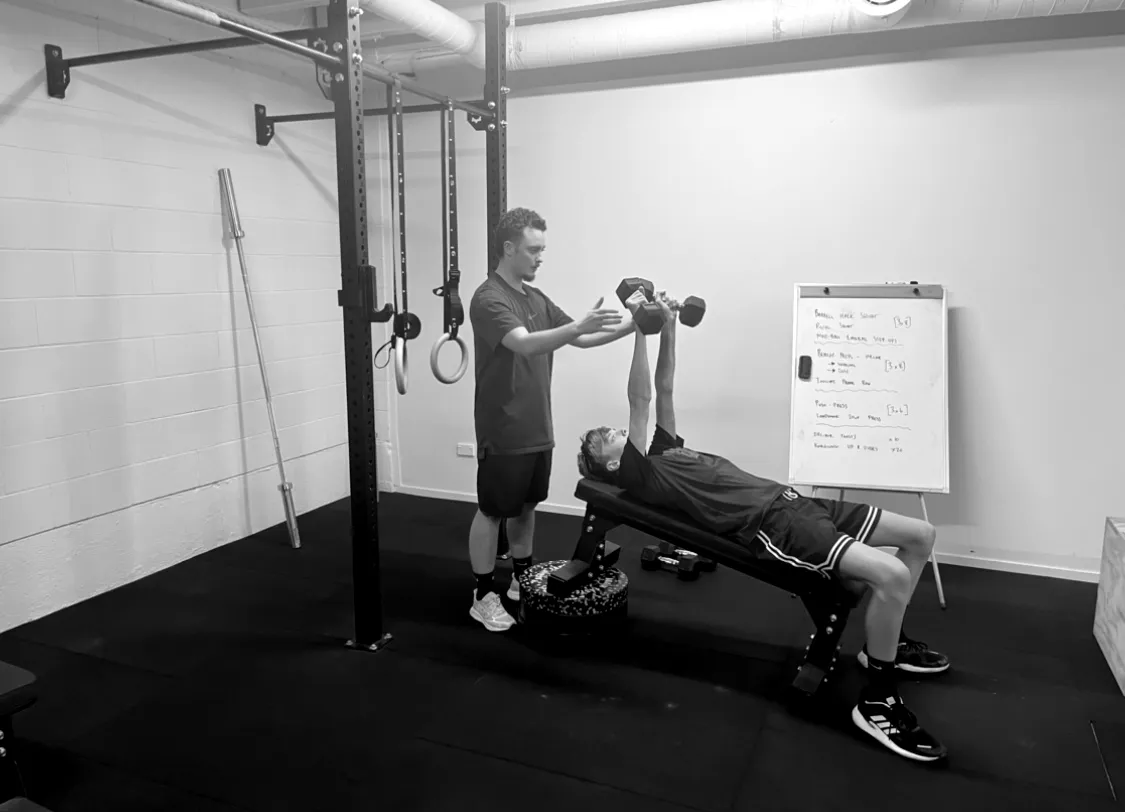 Siggy Brookland spotting a dumbbell press in the studio